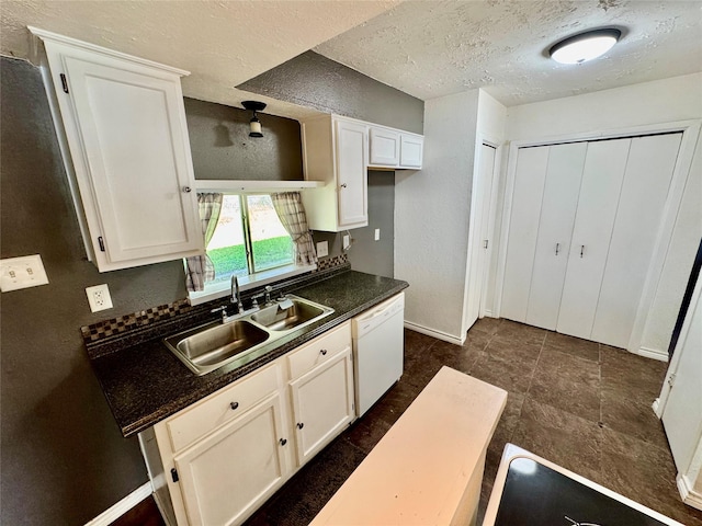 kitchen with dark countertops, white cabinets, white dishwasher, and a sink