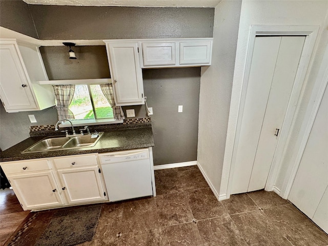 kitchen with a sink, dark countertops, white cabinets, and white dishwasher