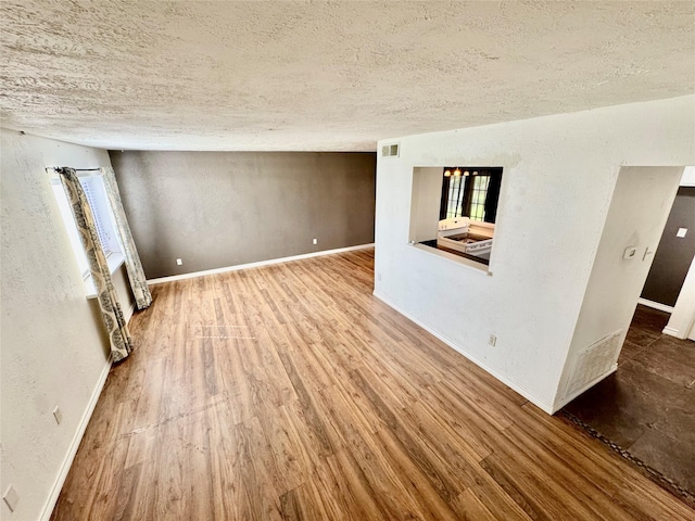 unfurnished room featuring baseboards, a textured ceiling, a textured wall, and wood finished floors