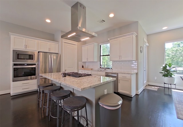 kitchen featuring island range hood, backsplash, white cabinets, and stainless steel appliances