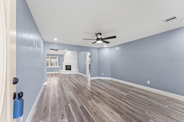 unfurnished living room featuring visible vents, baseboards, a fireplace, wood finished floors, and a ceiling fan