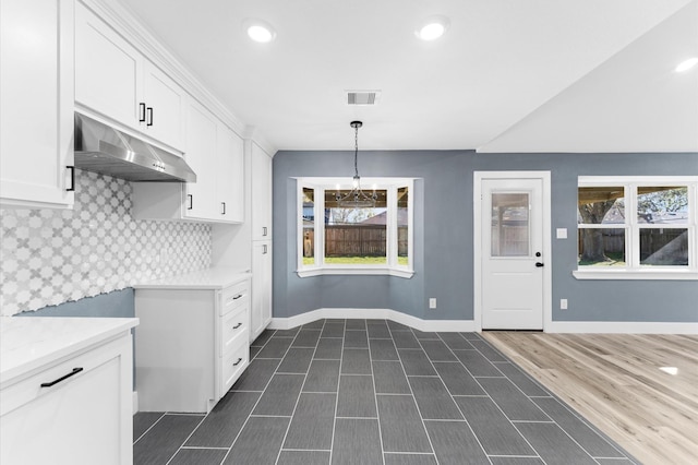 kitchen featuring tasteful backsplash, visible vents, baseboards, under cabinet range hood, and white cabinetry