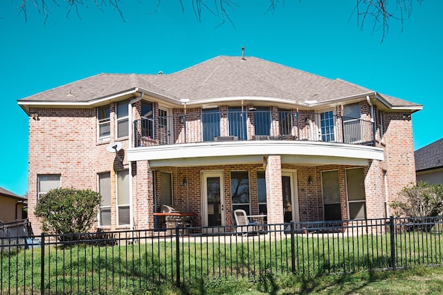 view of front facade featuring a front lawn, a balcony, a fenced backyard, and brick siding