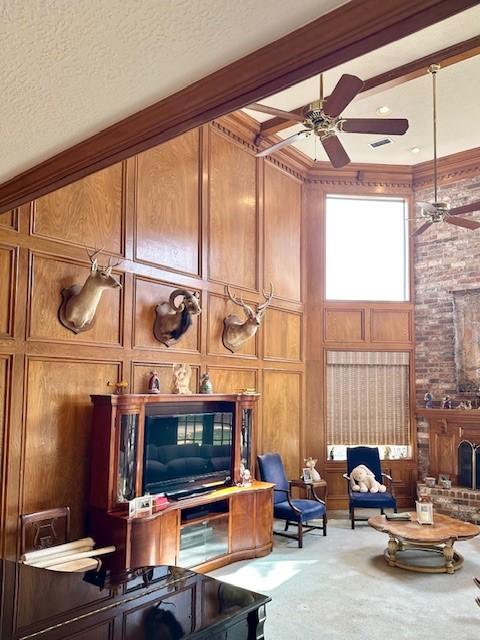 carpeted living room featuring a textured ceiling, a high ceiling, wood walls, and ceiling fan