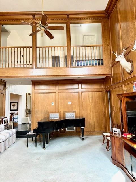 carpeted living area featuring a high ceiling, a ceiling fan, and wood walls