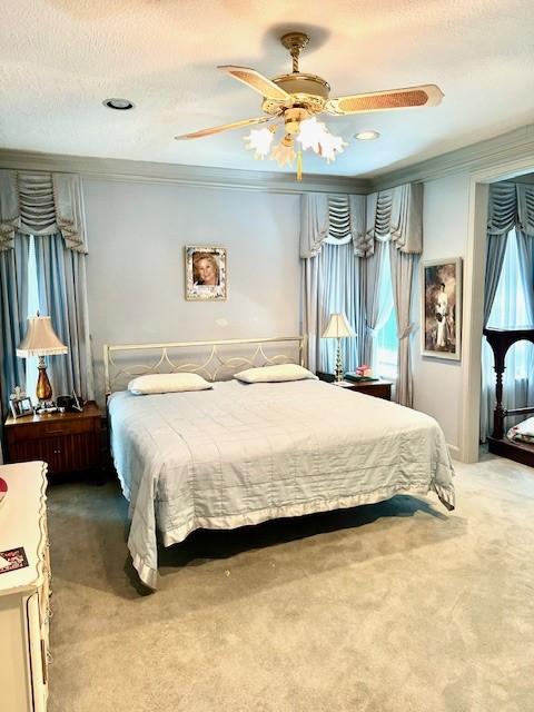 carpeted bedroom with a textured ceiling, ornamental molding, and a ceiling fan