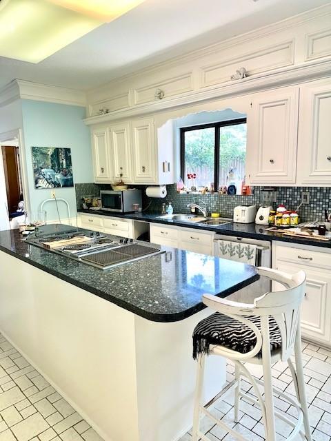 kitchen with stainless steel microwave, backsplash, ornamental molding, white cabinetry, and a sink