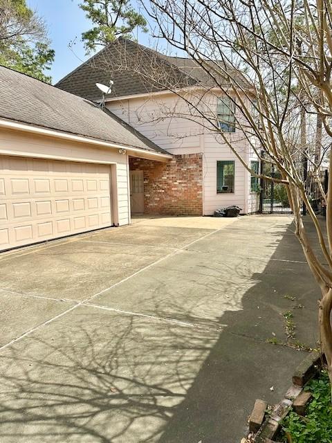 view of property exterior featuring an attached garage, concrete driveway, and roof with shingles