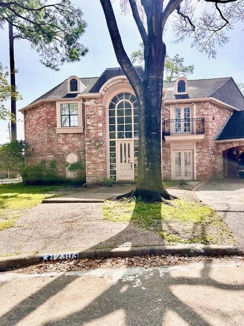 french country home featuring brick siding, french doors, a balcony, and fence