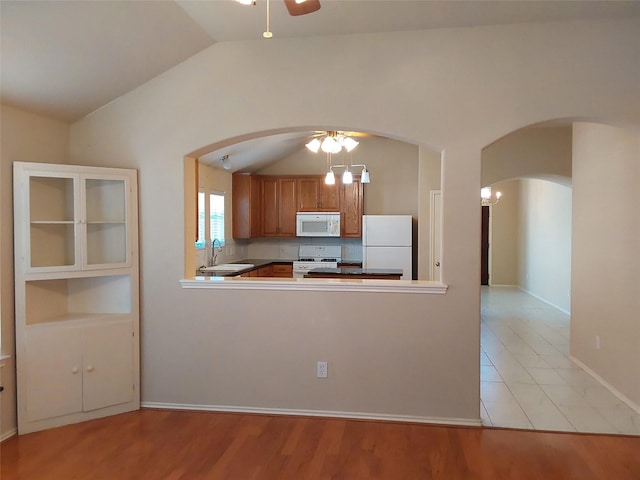 kitchen featuring white appliances, brown cabinetry, a ceiling fan, arched walkways, and a sink