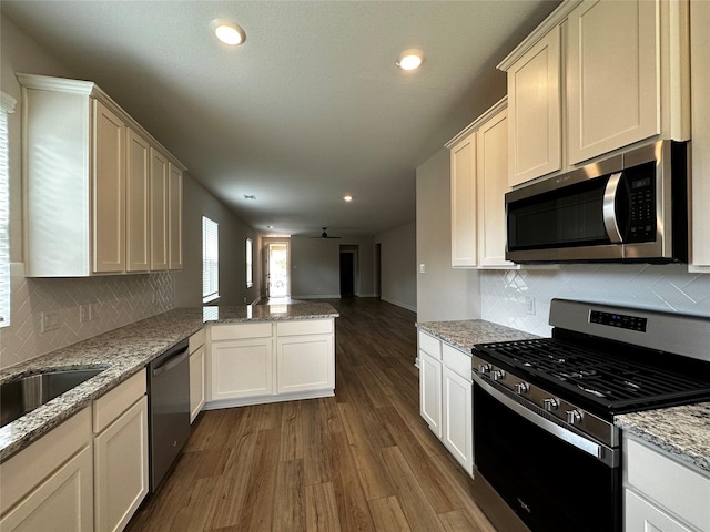 kitchen featuring dark wood-type flooring, open floor plan, decorative backsplash, appliances with stainless steel finishes, and a peninsula