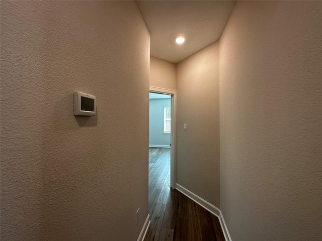 hall featuring dark wood-style floors, baseboards, and a textured wall