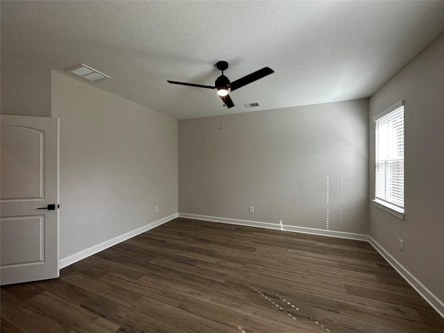 empty room with dark wood finished floors, a ceiling fan, visible vents, and baseboards