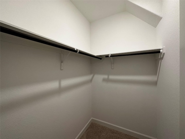 walk in closet with dark colored carpet and lofted ceiling