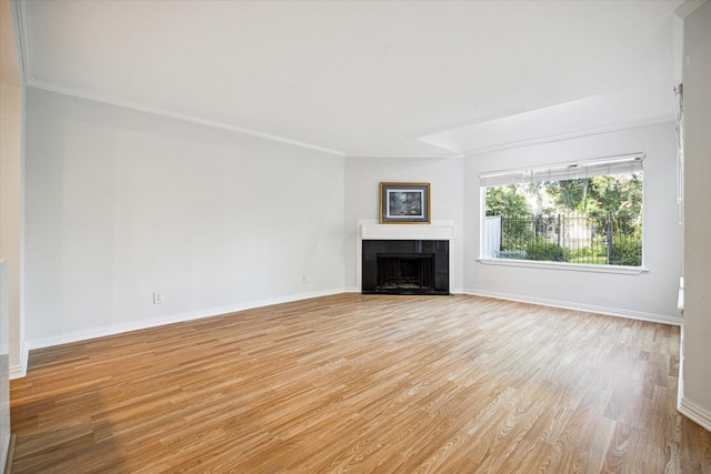 unfurnished living room with a tiled fireplace, baseboards, light wood finished floors, and ornamental molding