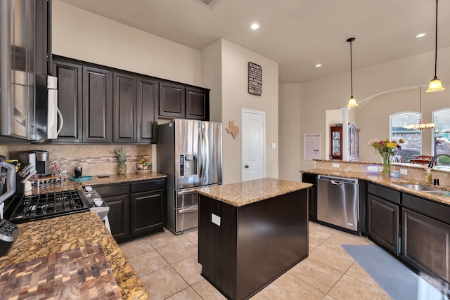 kitchen with light stone countertops, a kitchen island, a sink, stainless steel appliances, and tasteful backsplash