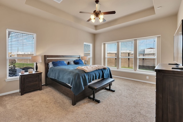 bedroom with ceiling fan, a tray ceiling, baseboards, and light carpet