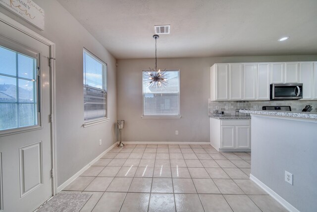 kitchen featuring visible vents, stainless steel microwave, white cabinets, decorative backsplash, and a chandelier