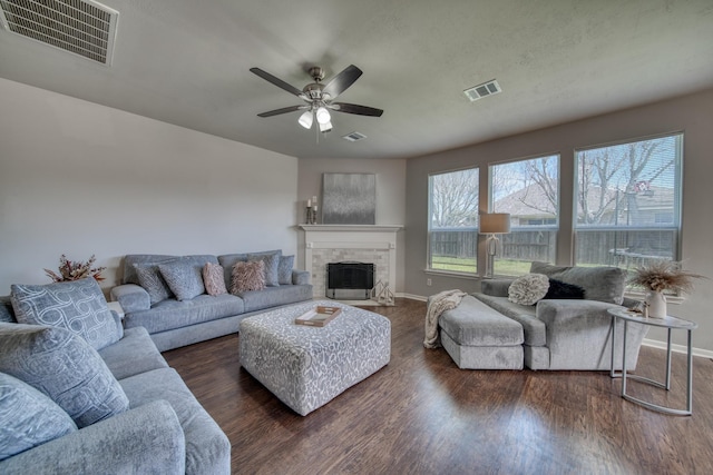 living area with visible vents, a stone fireplace, a ceiling fan, and wood finished floors