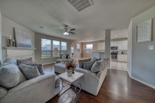 living room with visible vents, baseboards, dark wood-type flooring, and a ceiling fan