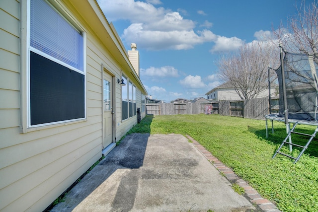 view of yard featuring a trampoline, a fenced backyard, and a patio area