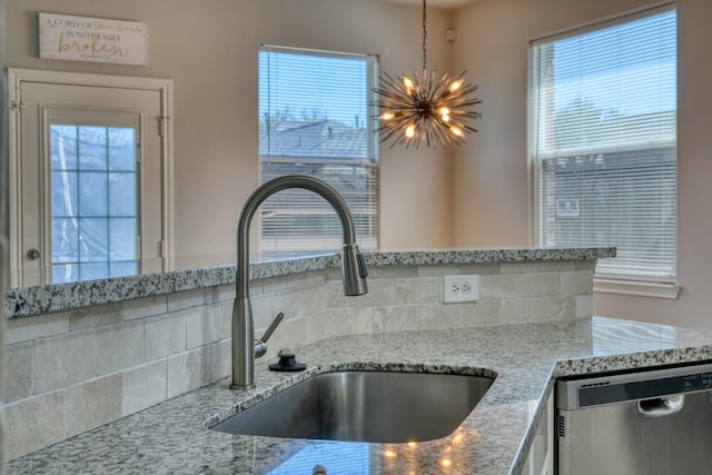 interior details featuring a sink, light stone countertops, stainless steel dishwasher, and a chandelier