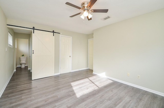 5343 Linda Ln, Katy, TX 77493 - unfurnished bedroom featuring visible vents, baseboards, a barn door, wood finished floors, and a ceiling fan