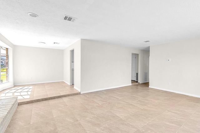 spare room featuring baseboards, visible vents, and a textured ceiling