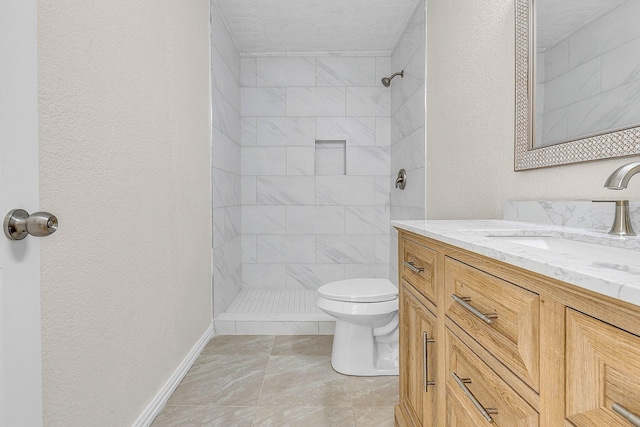 bathroom with toilet, vanity, a tile shower, a textured wall, and a textured ceiling