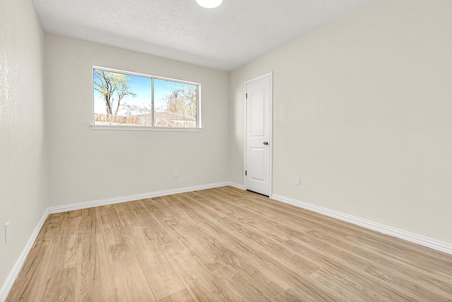 unfurnished room with light wood finished floors, a textured ceiling, and baseboards