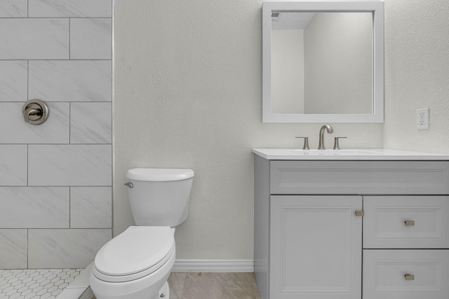 full bathroom with toilet, tiled shower, baseboards, vanity, and a textured wall