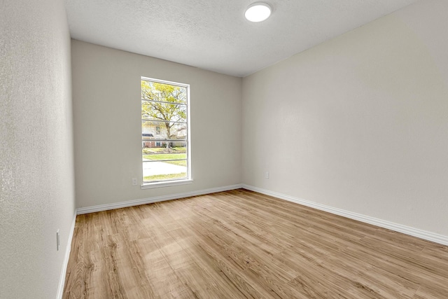 empty room with baseboards, a textured ceiling, and light wood-style floors