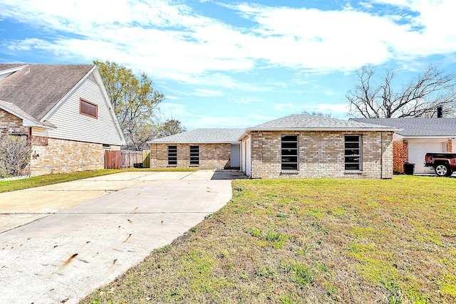 view of front of house with brick siding, a front lawn, fence, roof with shingles, and driveway