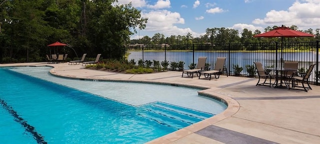 pool with a patio area, fence, and a water view