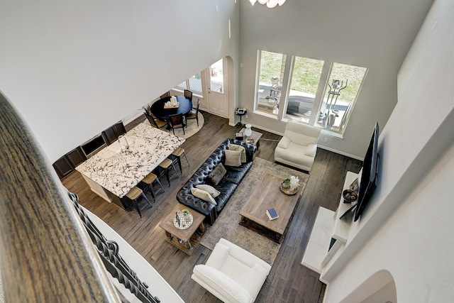 living room featuring arched walkways, baseboards, a towering ceiling, and wood finished floors