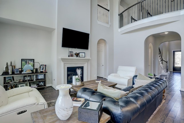 living room with stairway, wood finished floors, arched walkways, a towering ceiling, and a glass covered fireplace