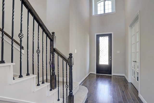 foyer entrance with stairway, a high ceiling, baseboards, and dark wood-style flooring