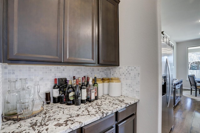 kitchen with wood finished floors, stainless steel fridge with ice dispenser, decorative backsplash, light stone countertops, and dark brown cabinets