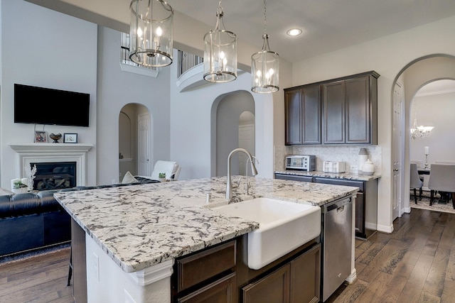 kitchen featuring dark wood-type flooring, stainless steel dishwasher, arched walkways, a notable chandelier, and a sink