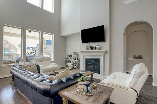 living area with a glass covered fireplace, baseboards, arched walkways, and dark wood-style floors