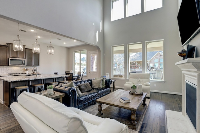 living room with visible vents, baseboards, a fireplace, arched walkways, and dark wood-style flooring