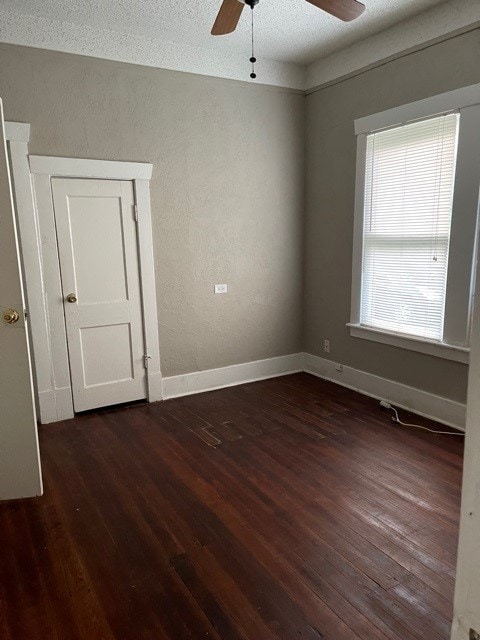 empty room with dark wood-style floors, baseboards, a ceiling fan, and a textured wall