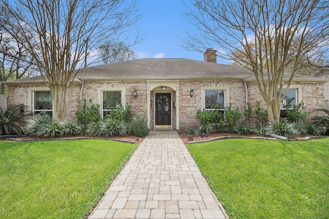 view of front of property with a chimney, brick siding, roof with shingles, and a front yard