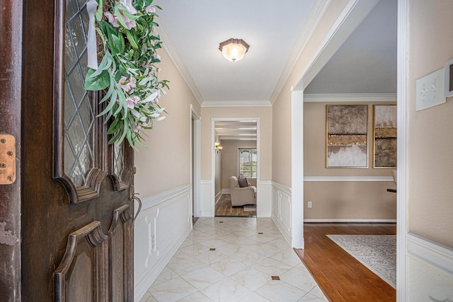 foyer with a wainscoted wall, crown molding, and a decorative wall