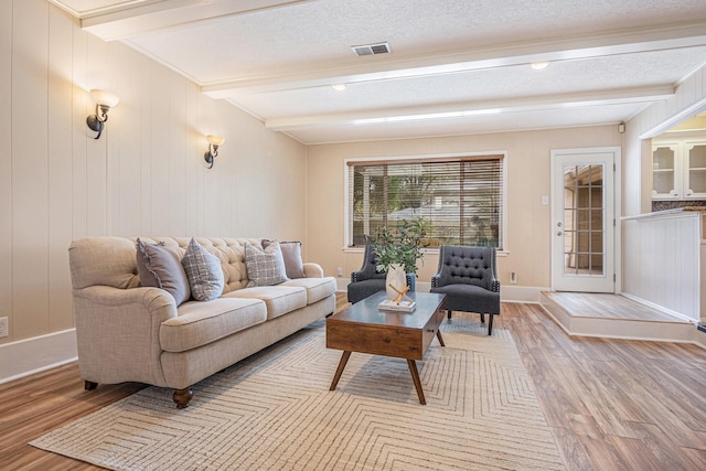 living room featuring light wood finished floors, visible vents, baseboards, beamed ceiling, and a textured ceiling