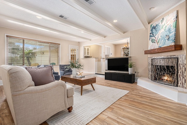 living area with visible vents, beam ceiling, a warm lit fireplace, wood finished floors, and a textured ceiling