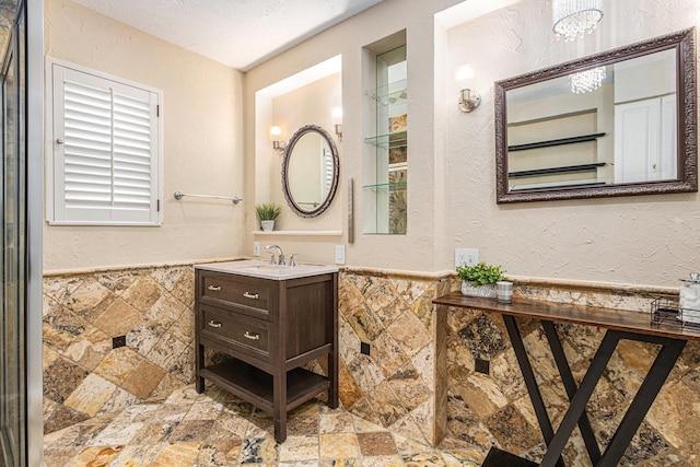 bathroom featuring stone tile floors, a wainscoted wall, a textured ceiling, and tile walls