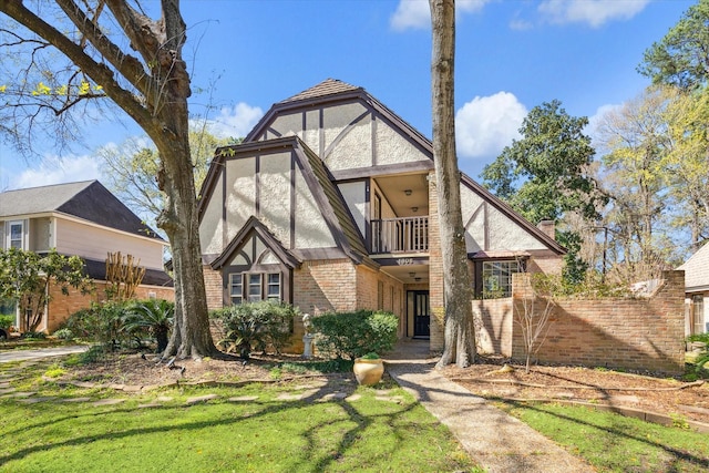 tudor-style house with stucco siding, a balcony, and brick siding