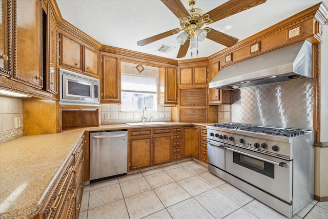 kitchen featuring visible vents, appliances with stainless steel finishes, brown cabinetry, wall chimney exhaust hood, and a sink