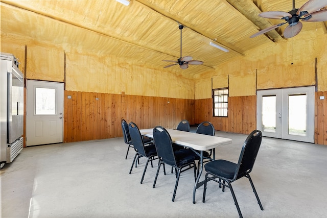 dining area with finished concrete floors, wood walls, french doors, and a ceiling fan